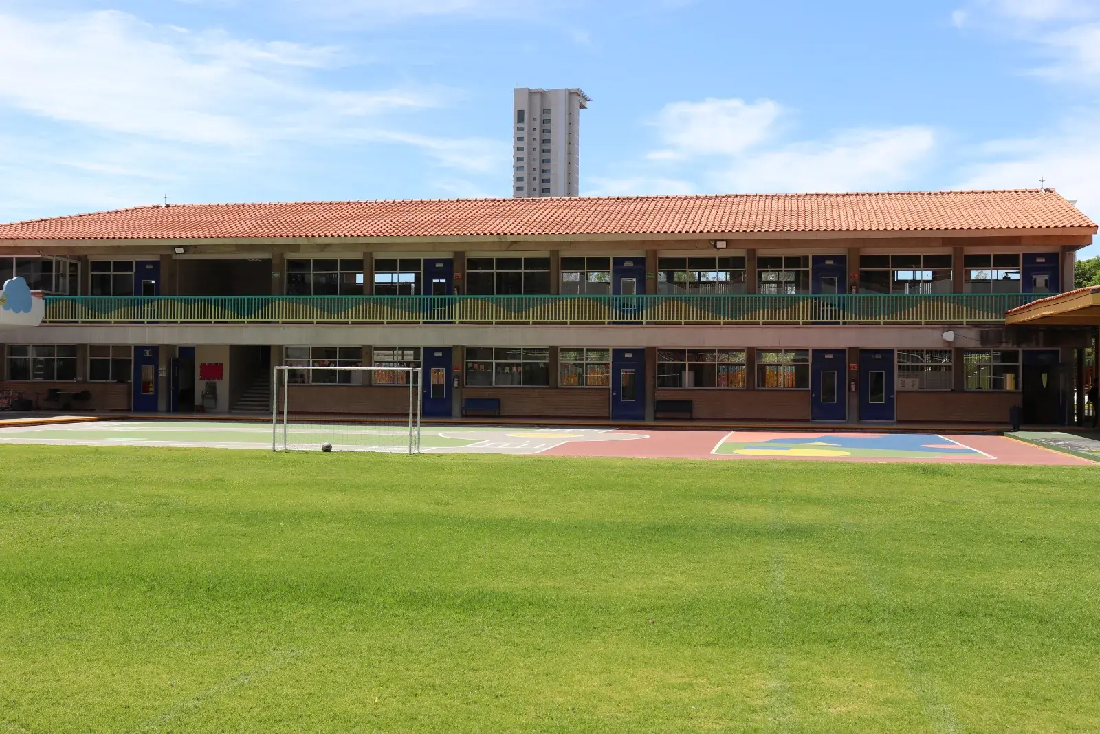 Edificio moderno de primaria con fachada colorida, amplios ventanales y terraza con piso de seguridad en área verde.